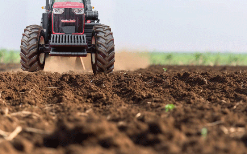 Foto sudut rendah dari traktor merah dengan bagian depan hitam dan kisi-kisi besar sedang membajak ladang.