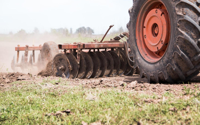 Traktor besar yang dilengkapi dengan ban bertapak berat yang bergerak dalam pengolahan lahan.