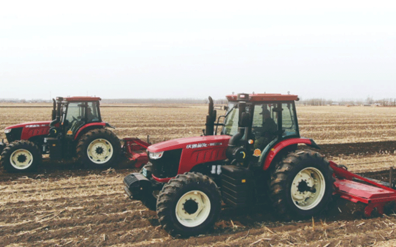 Dua traktor FMWorld merah sedang membajak di ladang.