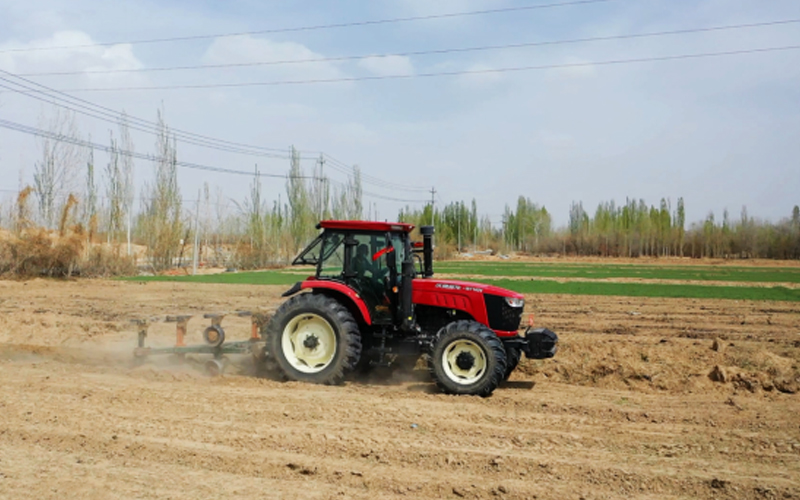 Traktor WF1404 berwarna merah mengolah lahan dengan pepohonan dan langit biru di kejauhan.